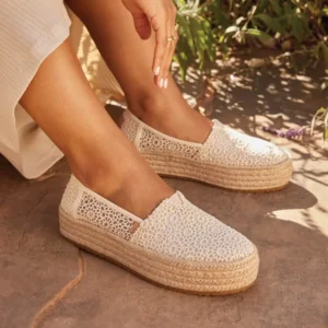 A woman's feet wearing white and beige TOMS shoes